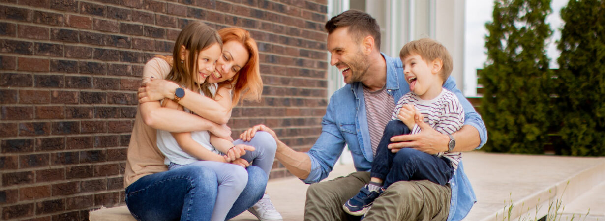 Family with a mother, father, son and daughter sitting outside o Family with a mother, father, son and daughter sitting outside on steps of a front porch of a brick house